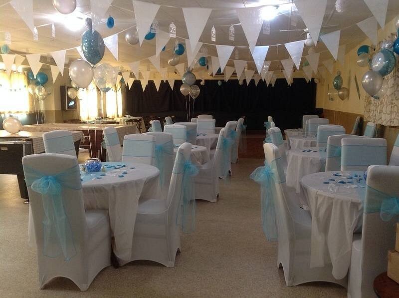 A function room set for a celebration, with dressed tables, blue chair sashes and bunting.